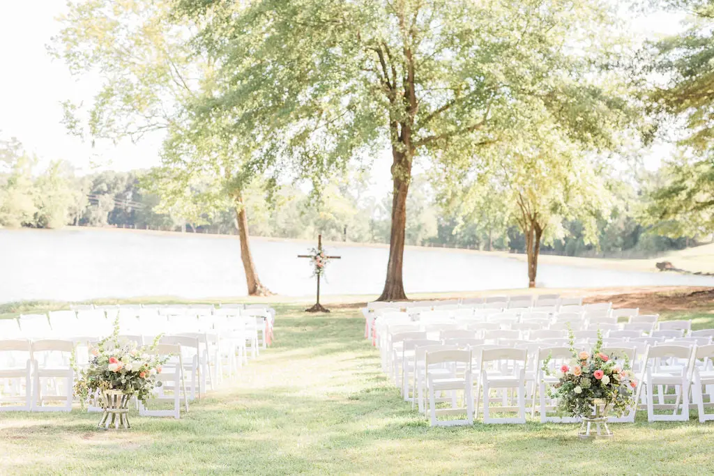 Outdoor wedding ceremony setup by the lake at Kick Back Ranch with white chairs and rustic decor.